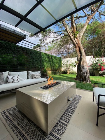 Fire table rectangular FIREPITSCR en terraza con pérgola, acabado claro pulido y llama lineal sobre lava.