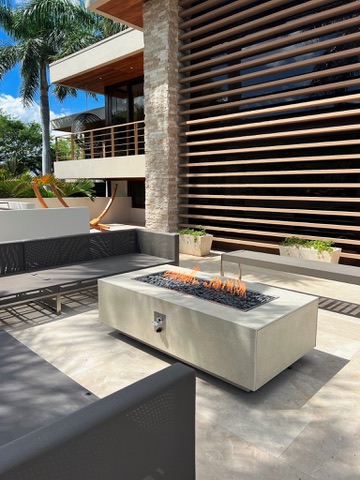 Fire table rectangular a gas FIREPITSCR en patio de lujo con sofás grises y arquitectura moderna.