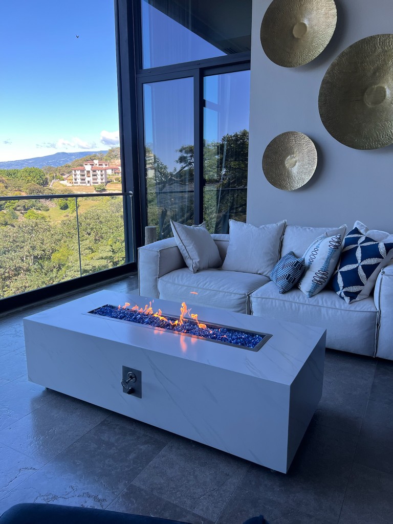 Fire table rectangular FIREPITSCR estilo mármol blanco con fire glass azul cobalto y vistas panorámicas.