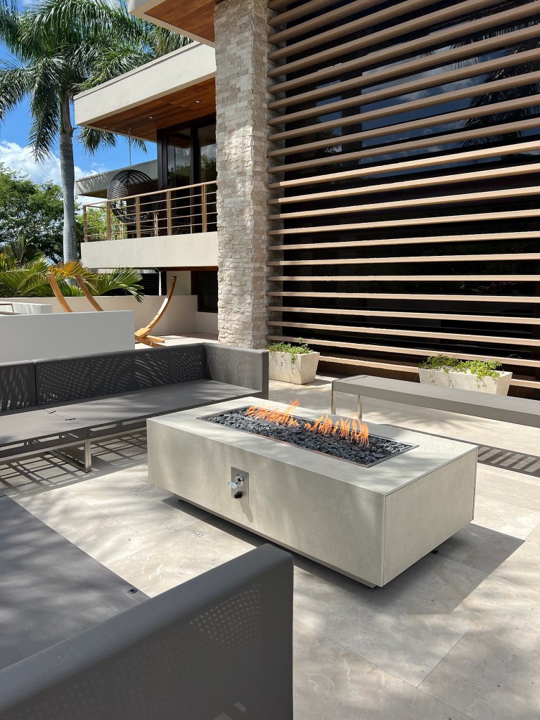 Fire table rectangular FIREPITSCR en terraza soleada rodeada de mobiliario exterior contemporáneo.